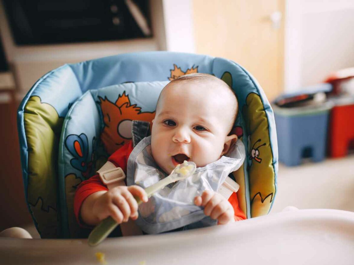 Bebe usando babador descartável enquanto come papinha no em sei cadeirão.