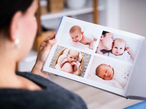 Mãe folheando um álbum de fotografias newborn de seu filho, relembrando os primeiros dias de vida do bebê. A imagem retrata um momento de afeto, memória e conexão.