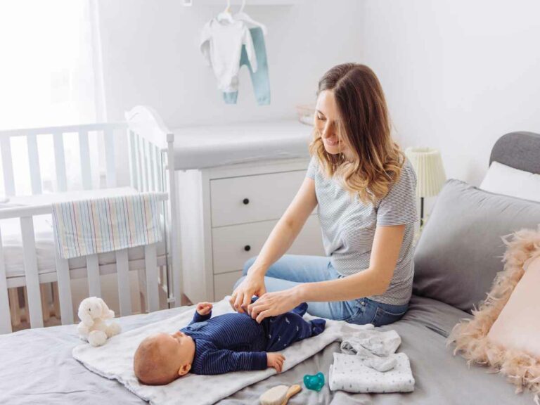 Mãe vestindo bebê com roupas estilosas, as quais foram escolhidas com o devido cuidado.