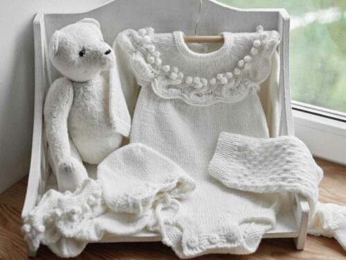 Roupa de batizado servindo como decoração para o quarto do bebê. As roupas brancas e o ursinho foram organizado em uma caixa de amostra.