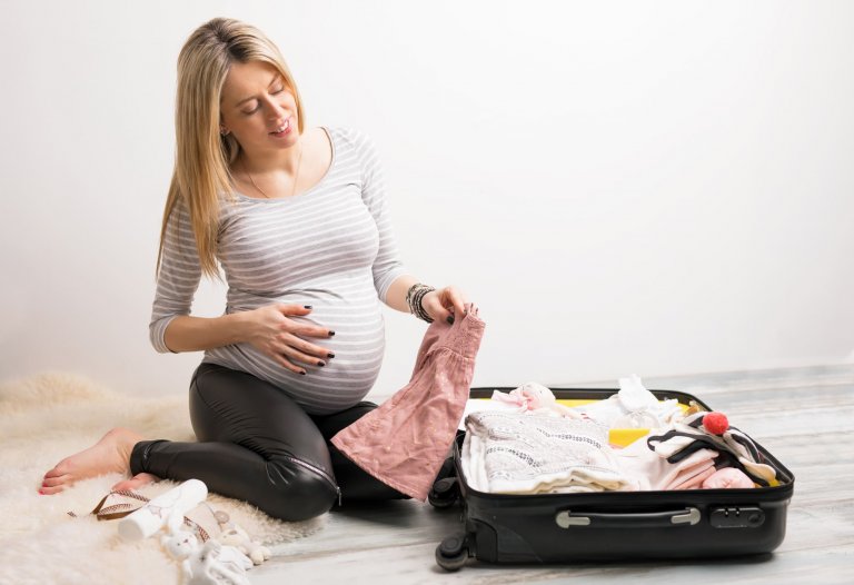 Mulher grávida sentada no chão com a mão na barriga, organizando mala maternidade
