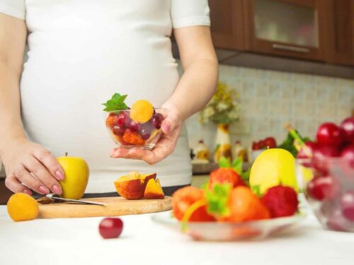 Mulher grávida montando um pote com as frutas ideias para a alimentação de gestante.