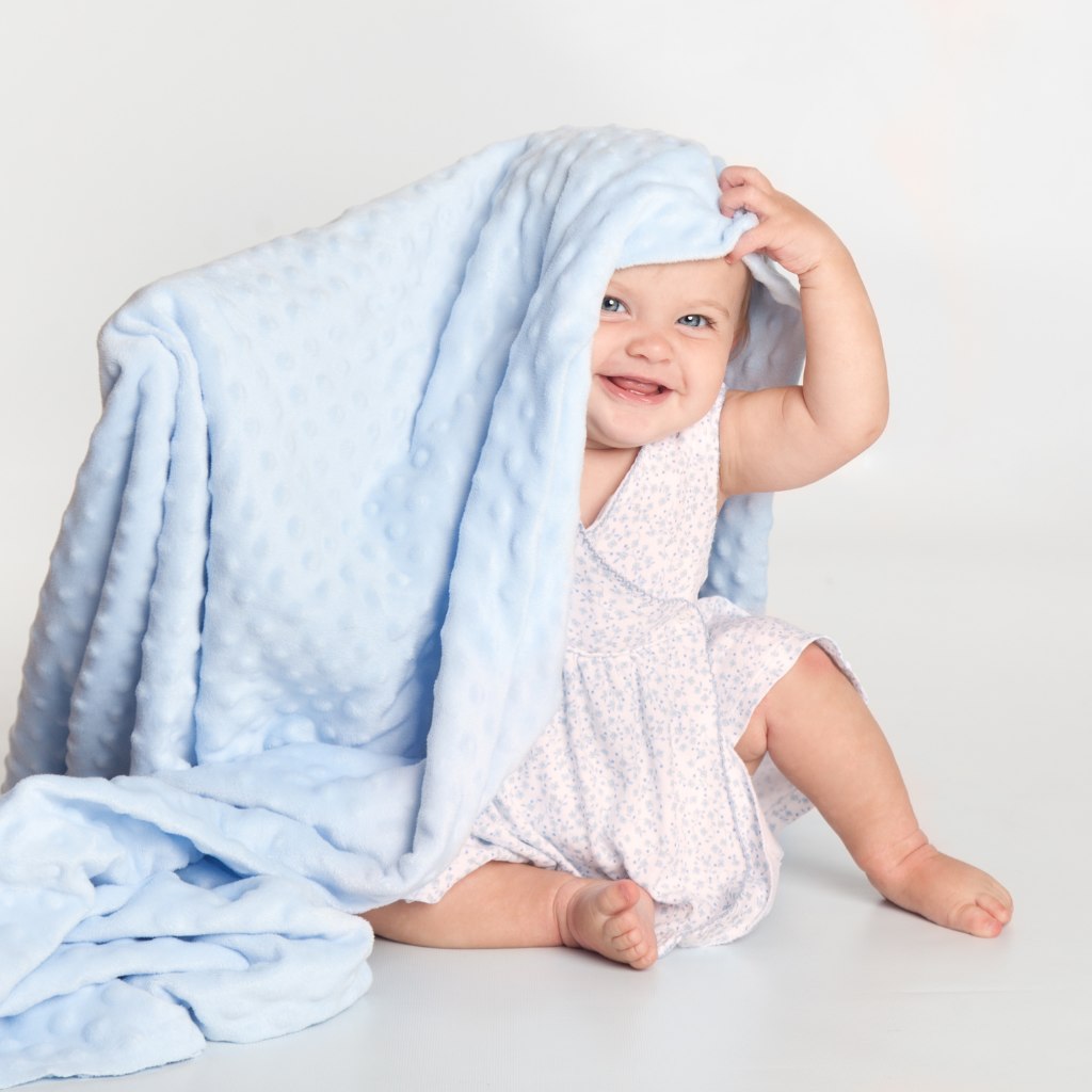 Bebê sorrindo brincando com uma manta de bebê azul em tecido soft