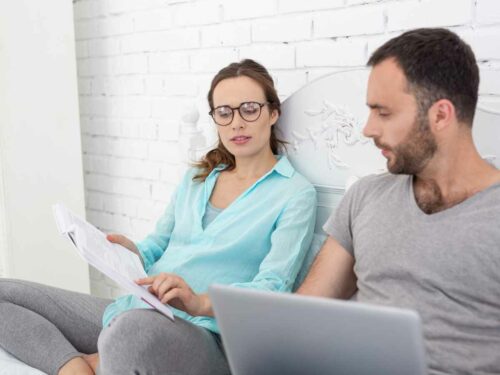 Casal grávido sentado lado a lado, com a mulher segurando um livro e o homem usando um laptop. Ambos estão concentrados estudando os principais desafios e cuidados na convivência entre pets e bebês, preparando-se para a nova fase em família.