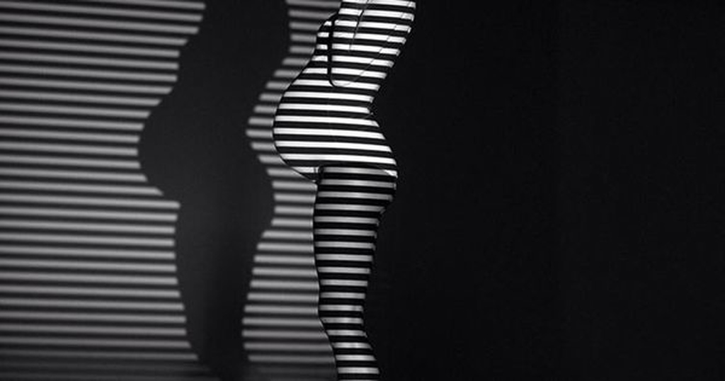 Foto de grávida em casa usando sombras para fazer efeito de linhas numa imagem preto e branca