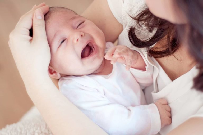 Bebê com cólica chorando emquanto mãe passa mão sobre sua cabeça. bebês transpiram cabeça