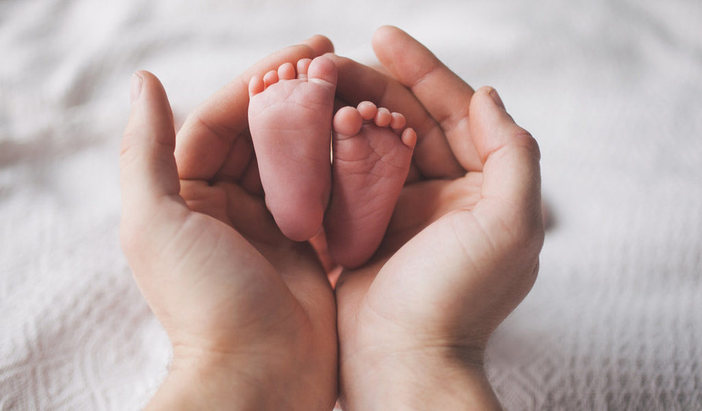 Mãos de mãe segurando os pés de bebê recé-nascido ilustrando como preprar a chegada de um bebê