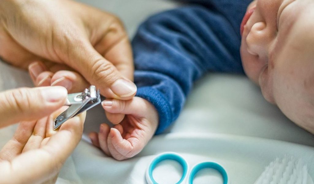 Mãe cortando unha de bebê menino usando tesourinha azul