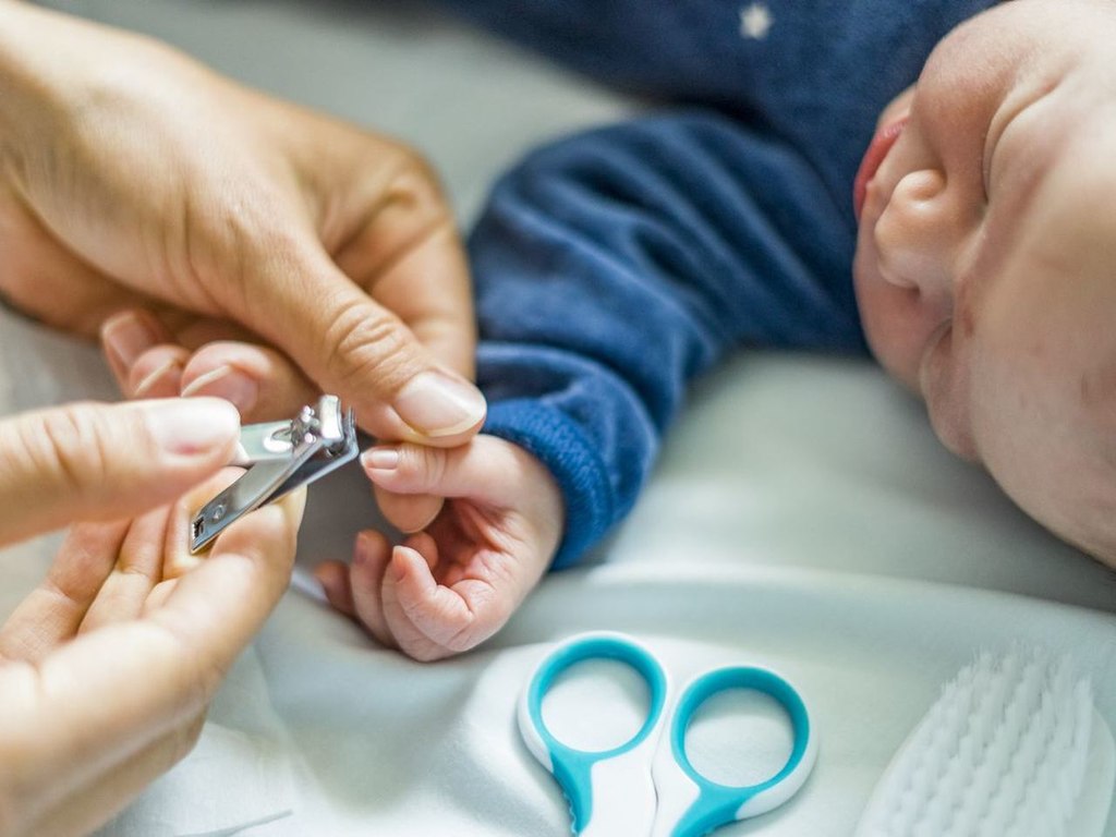 Mãe cortando unha de bebê menino usando tesourinha azul