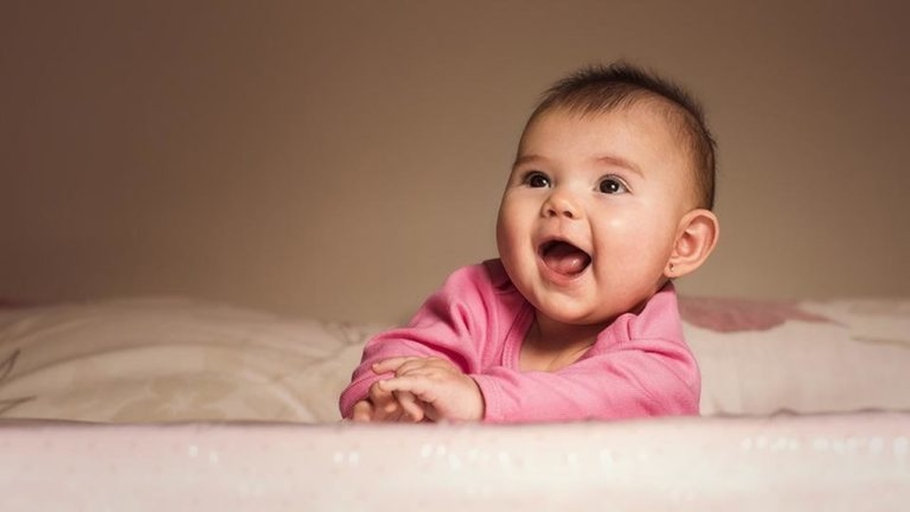 Imagem mostra bebê vestindo body rosa sorrindo com aspecto de empolgação.