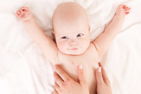 Massagem em bebê Mãe fazendo massagem em bebê com os braços para cima sobre a cama