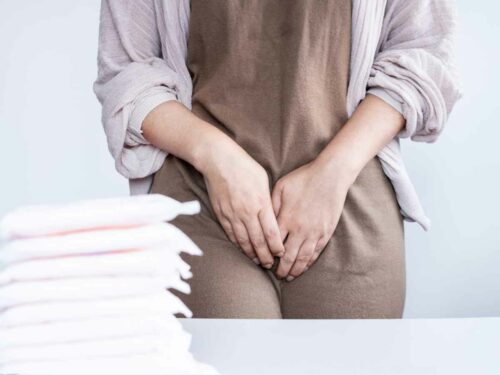 Mulher passando pelo resguardo com o sintoma de sangramento vaginal conhecido como lóquios. A mulher está com um pilha de absorventes em sua frente.