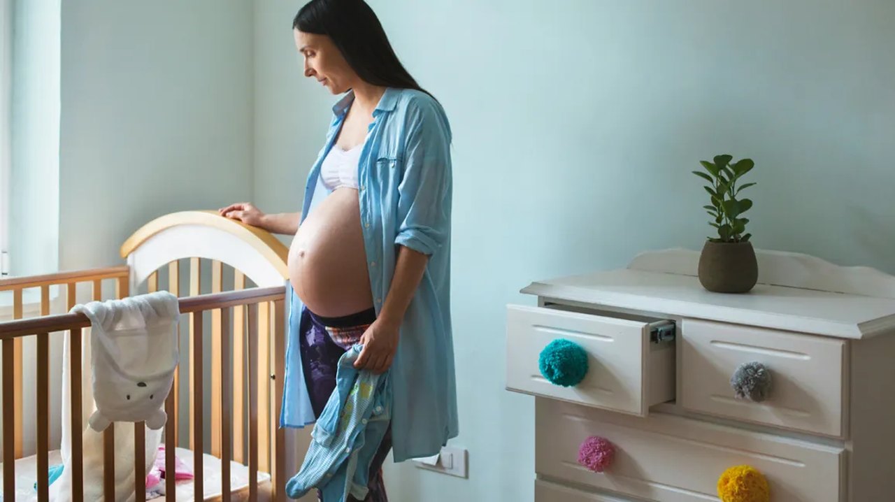 mulher grávida do lado do berço, mãe de primeira viagem pensando no que comprar para o bebê