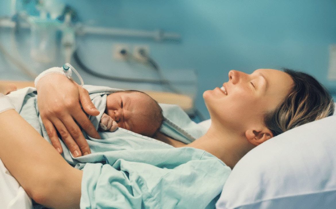 Mamãe deitada segurando bebê recém nascido na maternidade