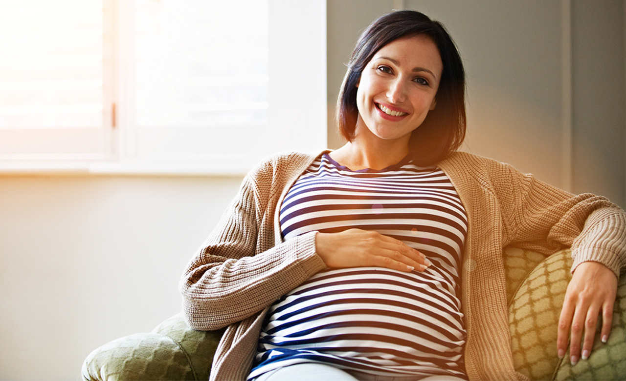 Grávida sorrindo, com a mão sobre a barriga, simbolizando a diferença entre gravidez de menino e menina