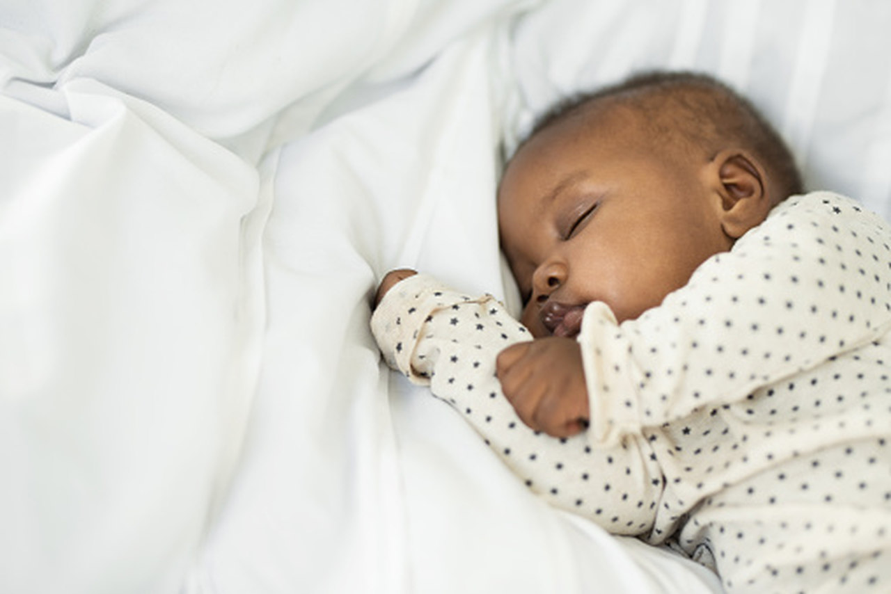 Bebê dormindo pacificamente, com uma roupinha de cor creme com pequenas estrelinhas