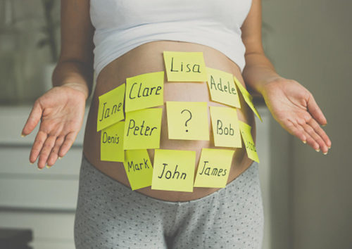 Barriga de grávida com post its com ideias de nomes para bebe, como Lisa, Adele, Clare, Jane, Peter (Pedro), Denis, Mark, John (João), Jame e Bob e um central com ponto de interrogação. A grávida está com as palmas da mãos abertas, apontadas para cima, simbolizando dúvida