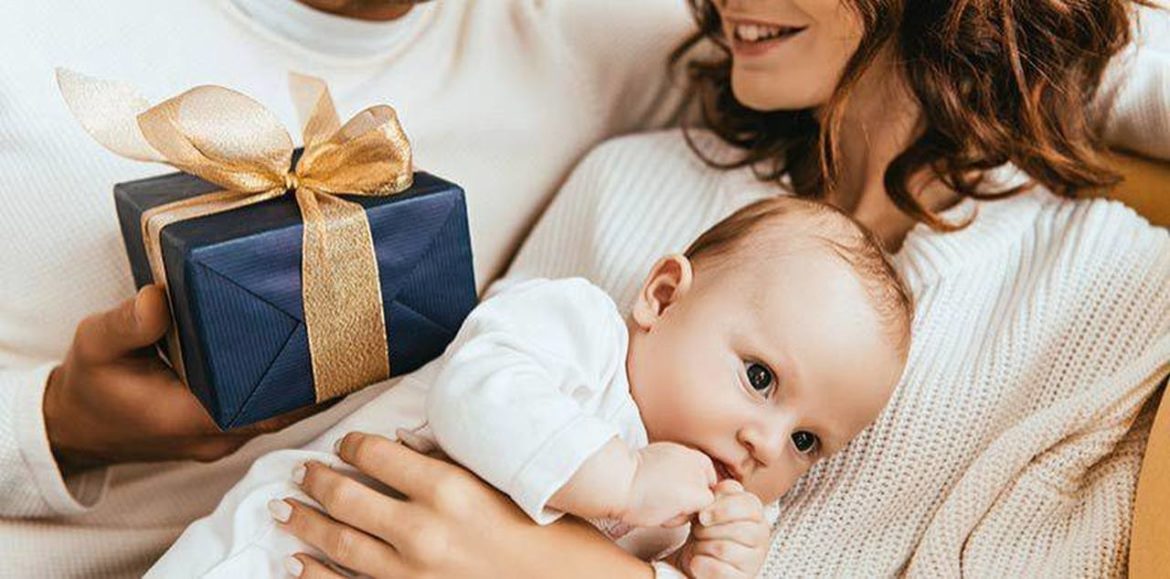 Bebê no colo da mãe, que está sorrindo recebendo um presente, simbolizando kit presente para bebê recém-nascido