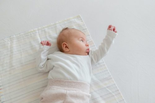 Bebê sobre lençol, com mãozinha pra cima e blusa de manga comprida, simbolizando dicas de como saber se bebê está com frio