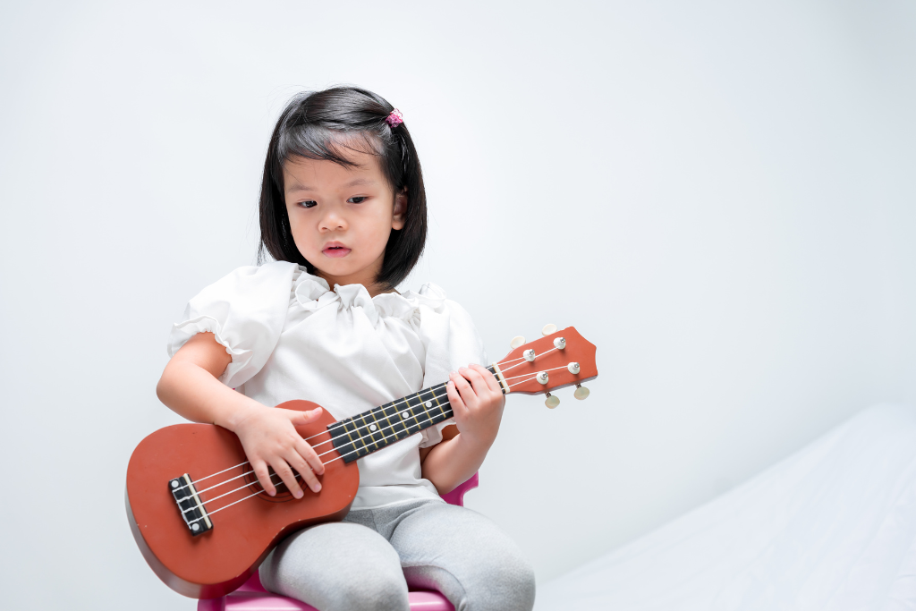 Menina sentada segurando um Ukulele na mão, tentando tocar.