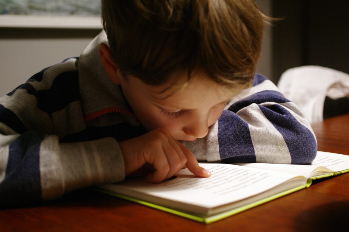 Criança lendo livro apoiada em uma mesa