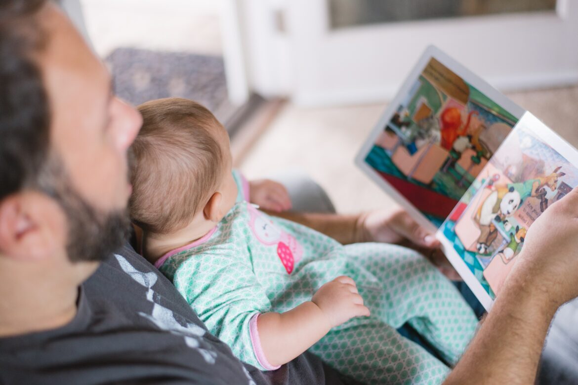 Pai lendo livro de histórias para um bebê em seu colo