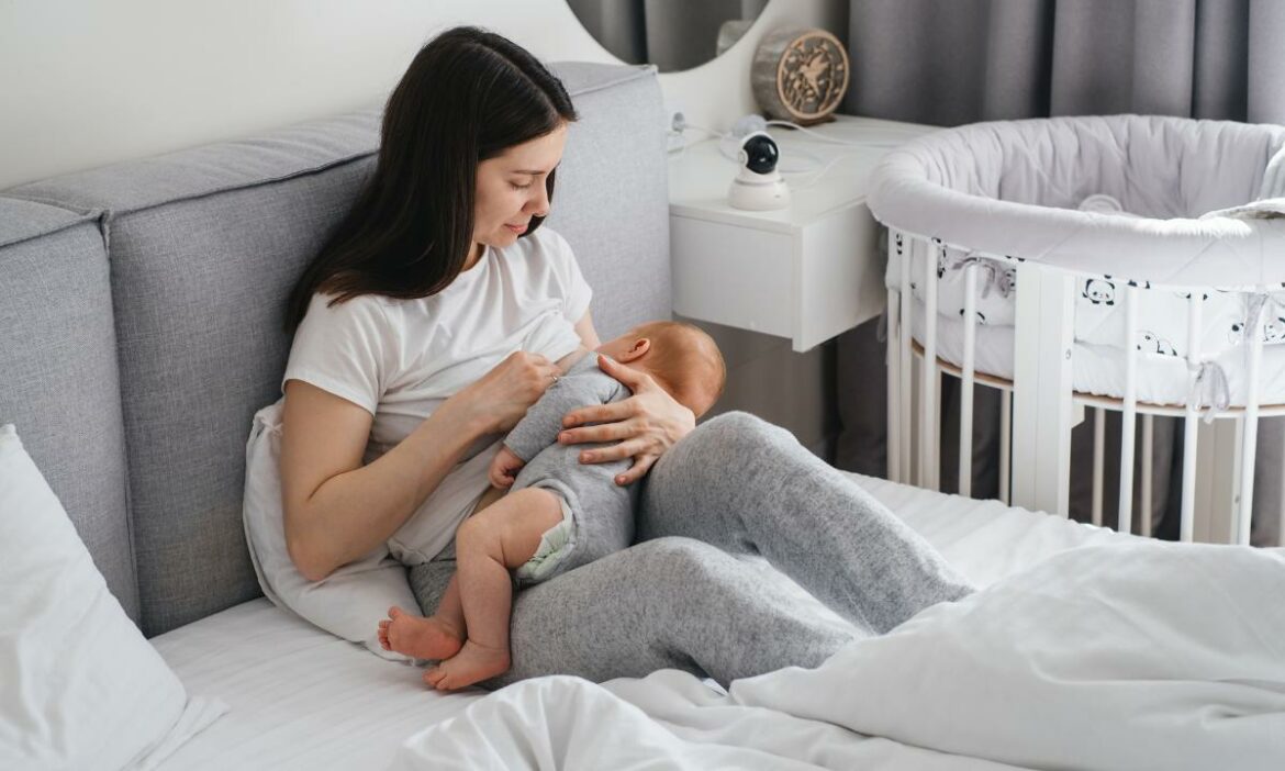 mãe com seu filho na cama amamentando-o. Ao lado o berço da criança. Escolha do local para o espaço de amamentação