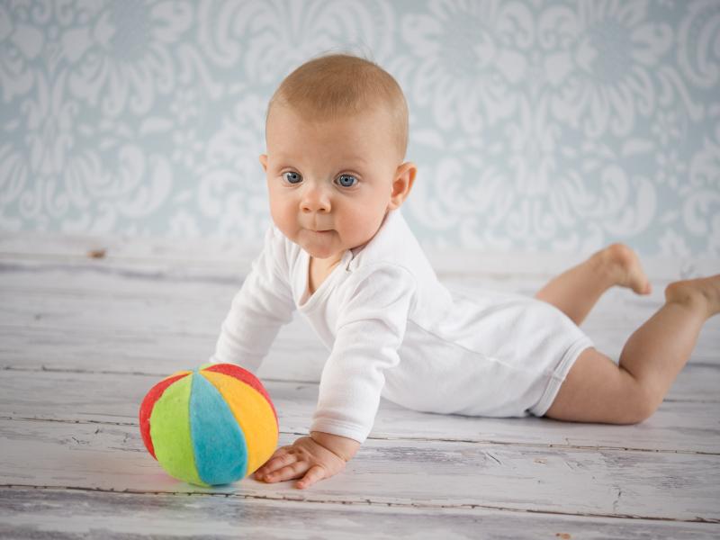 bebê brincando com bola coloria no chão