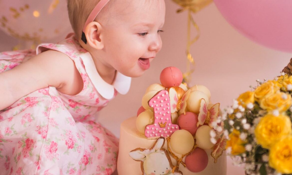 Bebê muito feliz com seu bolo de aniversário cor de rosa, e algumas flores amarelas ao lado