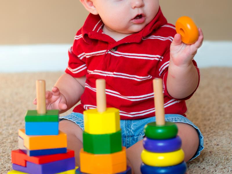 bebê sentado brincando com brinquedo de encaixe colorido