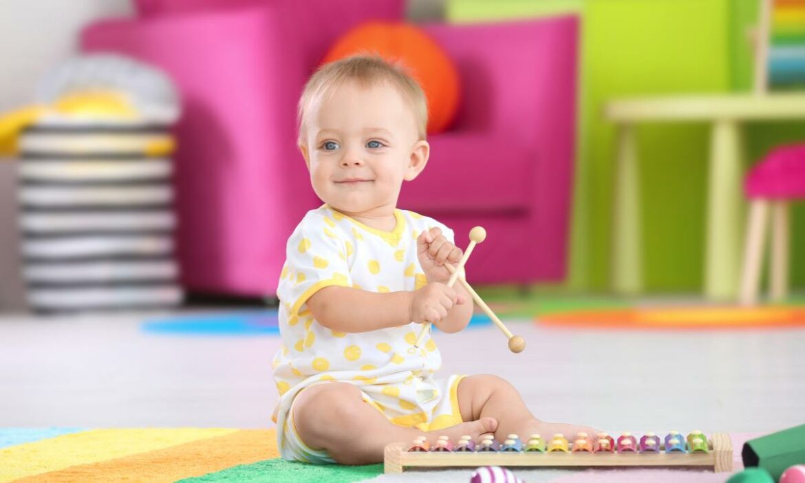 Bebê usando a música no desenvolvimento, sentado no chão com baqueta e instrumento de toque a sua frente