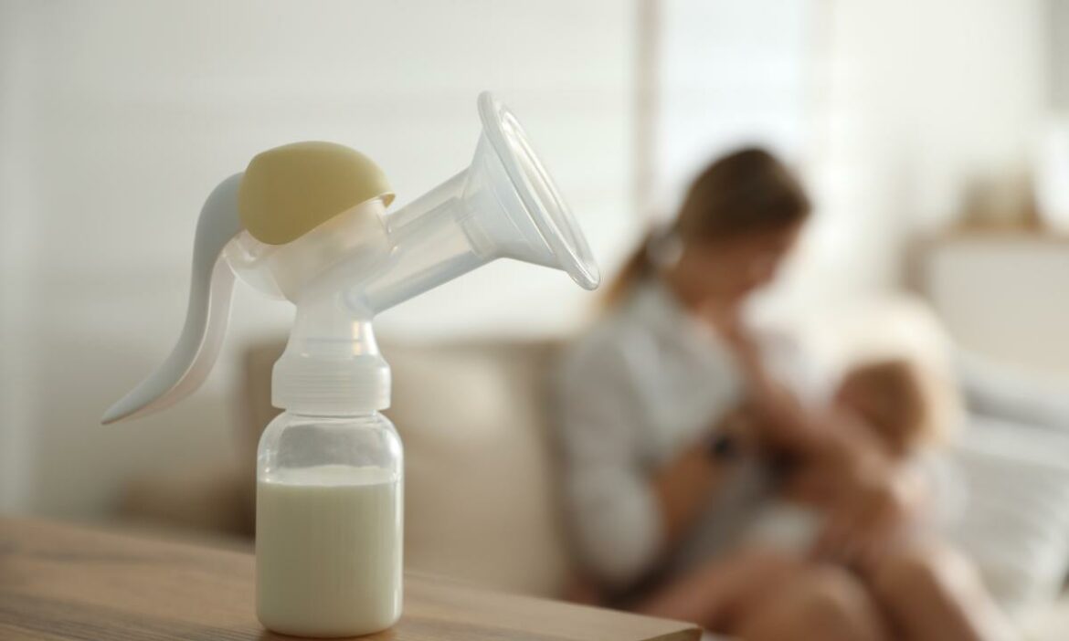 Bomba de extração de leite e uma mãe amamentando seu bebê ao fundo