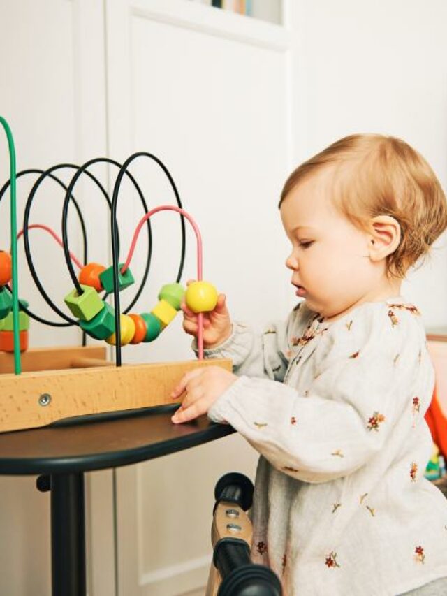 bebê em pé brincando com brinquedo de formas coloridas sobre a mesa