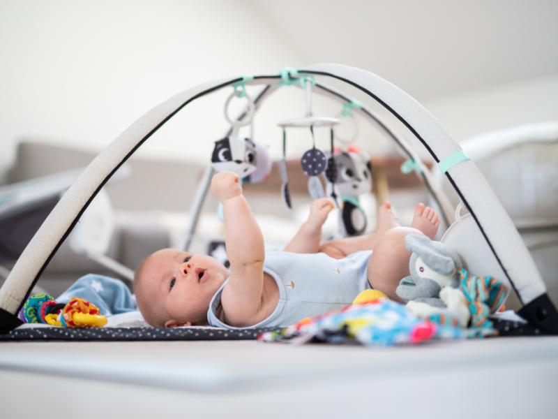 bebê deitado brincando com brinquedo que contém formas penduradas para estimular a criança e mostrando os marcos do desenvolvimento do bebê