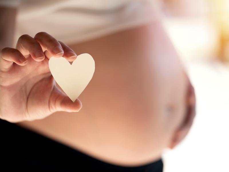 mulher grávida segurando um coração de papel na mão