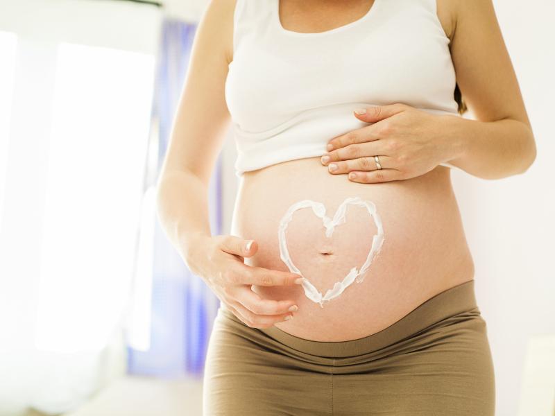 mulher grávida passando creme em sua barriga em forma de coração