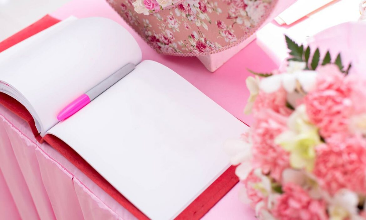 Agenda usada para fazer lista de convidados de uma festa, sobre a mesa cor de rosa. Flores desfocadas ao lado