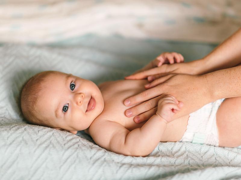 bebê de olho claro deitado e sendo massageado na barriga