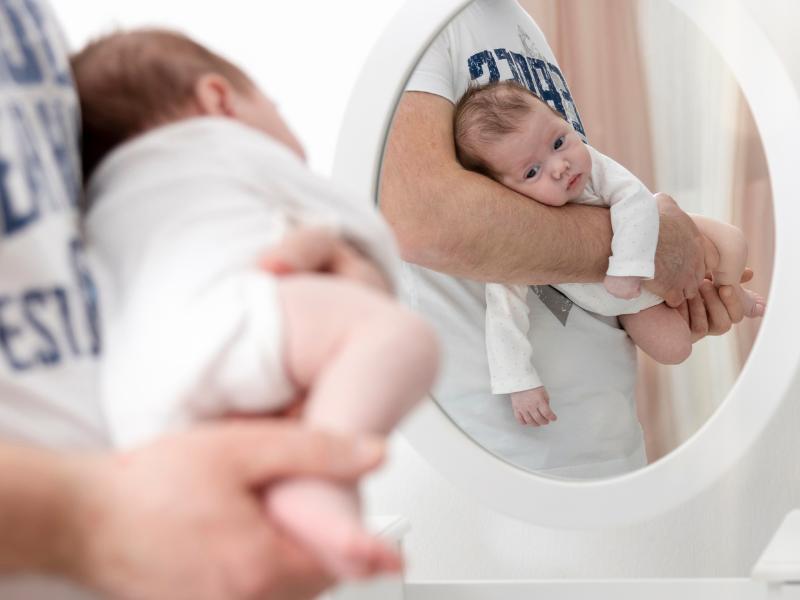bebê deitado no antebraço do pai e reflexo desta ação aparece no espelho