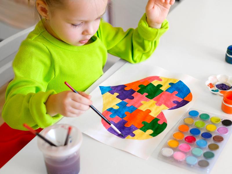criança pintando desenho colorido em formato de coração sobre a mesa com pincel e tinta