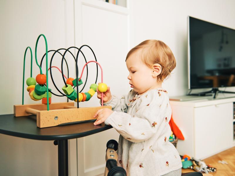 bebê em pé brincando com brinquedo de formas coloridas sobre a mesa
