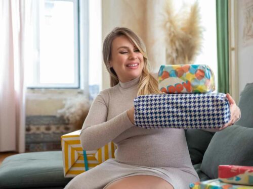 Mulher grávida sorridente sentada no sofá segurando presentes embrulhados.