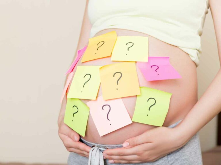 Mulher grávida com a barriga coberta por post-its coloridos com pontos de interrogação, simbolizando a escolha do nome do bebê.