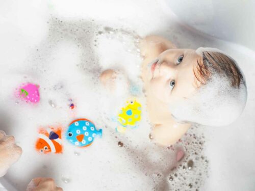 Bebê tomando um banho divertido na banheira cheia de espuma e brinquedos aquáticos.