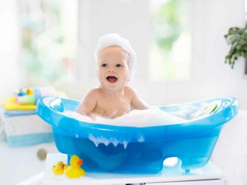 Bebê na hora do banho se divertindo com a espuma da banheira e os brinquedos aquáticos.