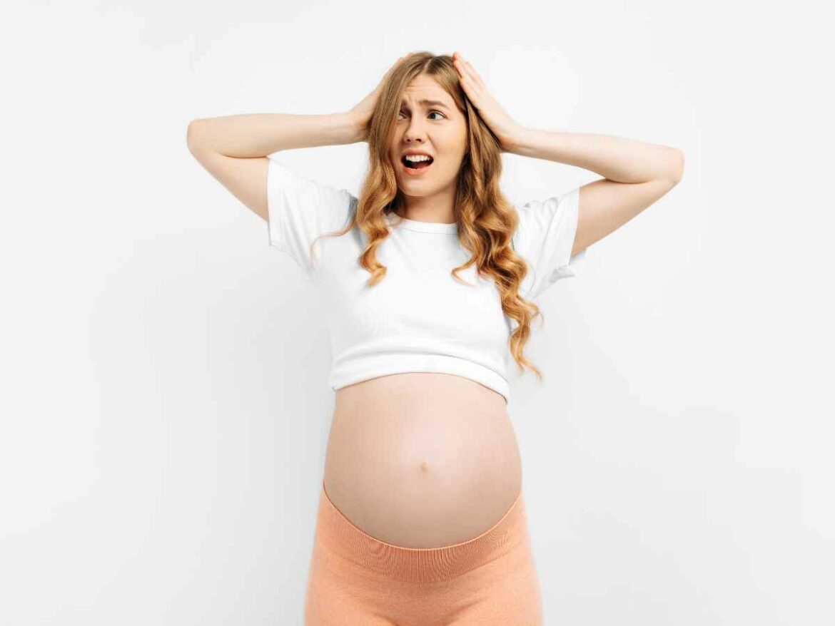 Grávida com as mãos na cabeça e uma expressão de nervoso, como se estivesse se sentido ansiosa.