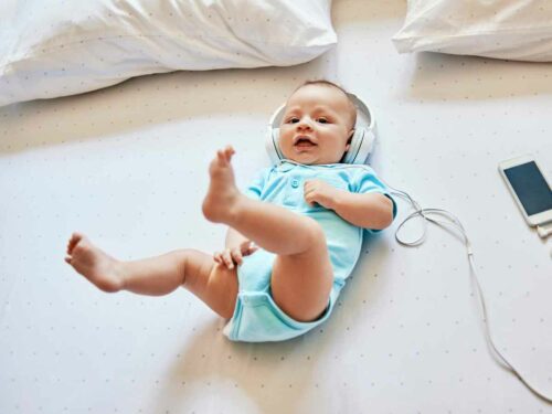 Bebê deitado, usando fones de ouvido enquanto escuta música e tenta mover as perninhas como se estivesse acompanhando o ritmo, demonstrando encantamento e resposta natural aos estímulos sonoros.