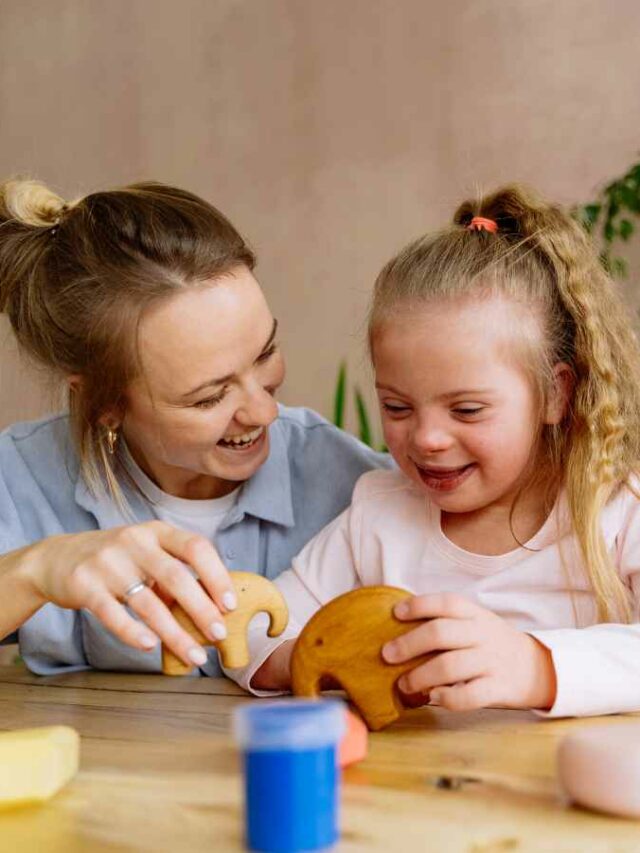 Mãe estimulando sua filha com atraso de desenvolvimento por meio de uma brincadeira com peças de madeira. As duas sorriem durante a atividade, criando um momento de aprendizado, conexão e alegria.