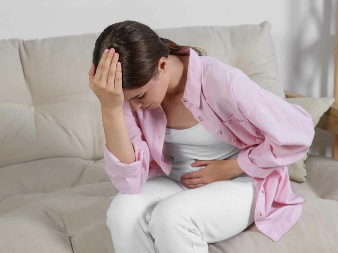 Mulher com febre no pós-parto, por não ter cuidado corretamente da sua infecção urinária. Ela está sentada no sofá com a mão na testa.