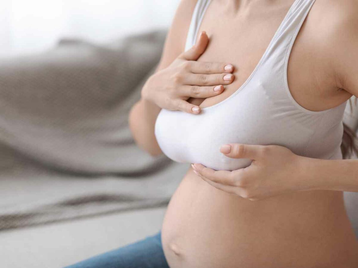 Mulher no puerpério apalpando o próprio seio com cuidado, enquanto passa pela fase de descida do leite. A imagem retrata um momento comum do pós-parto, marcado por mudanças hormonais, sensibilidade mamária e o início da amamentação.